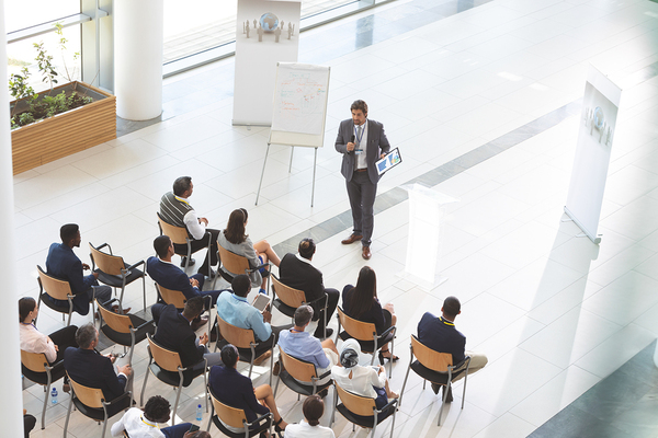 Conference speaker using a mic and document to present information to an audience.