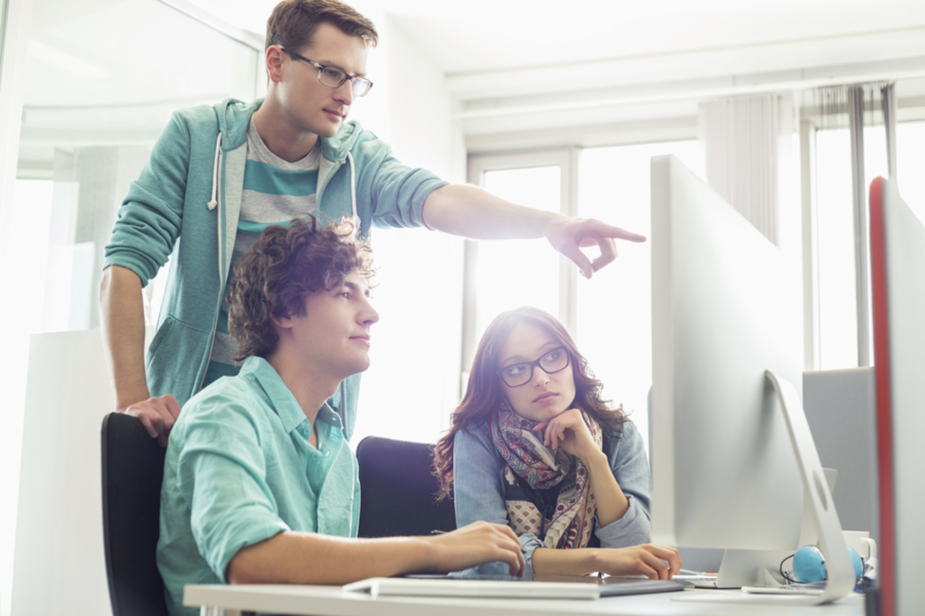 Group of coworkers discussing a project in front of a desktop computer.