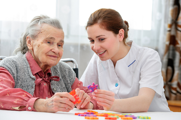 Physical therapy working with an elderly woman at a table with foam puzzle pieces.