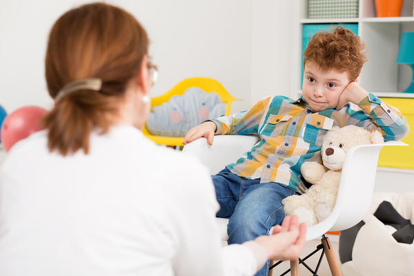 Young boy with a teddybear talking with a therapist.