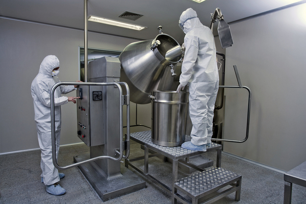 Two workers with white protective gear cleaning a machine.