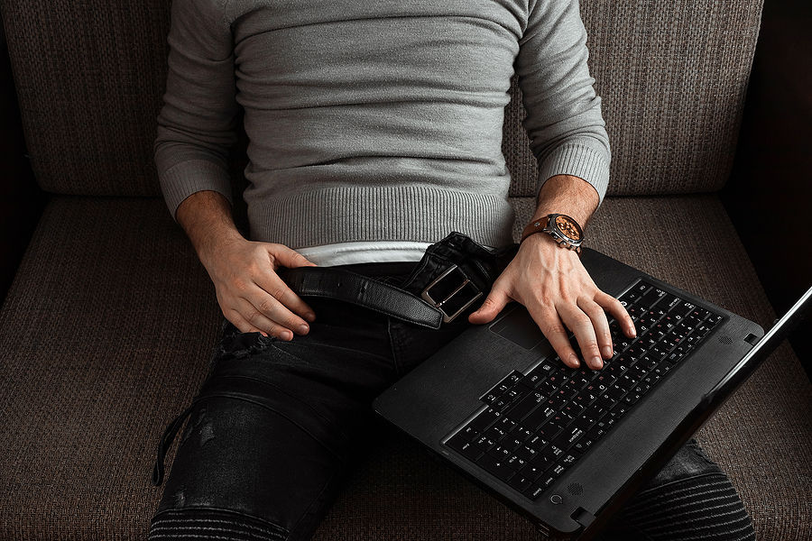 Man sitting on a couch with a laptop on his lap.