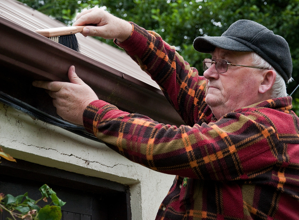 Older man cleaning out his gutters with a brush.