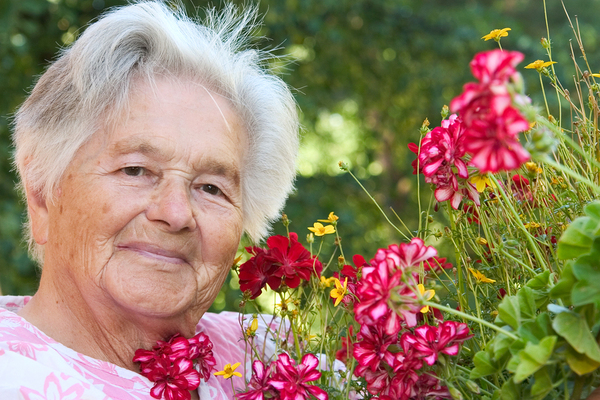 Older woman standing next to dark pink flowers.