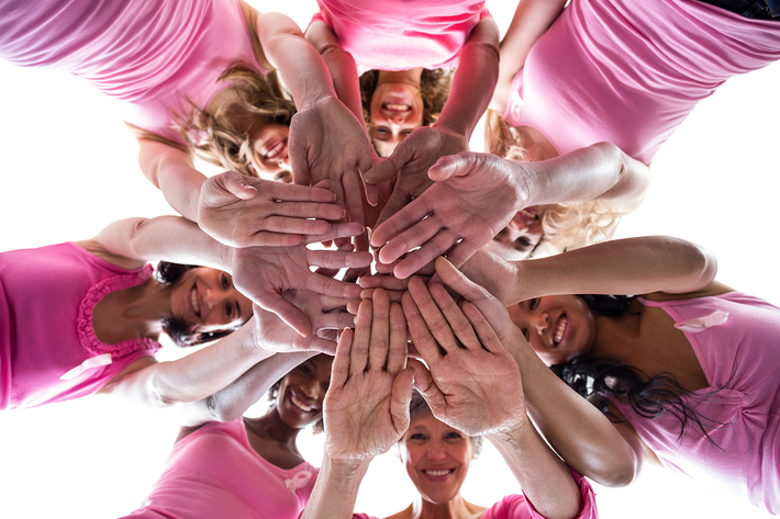 Group of women with pink shirts placing their hands together in a circle.