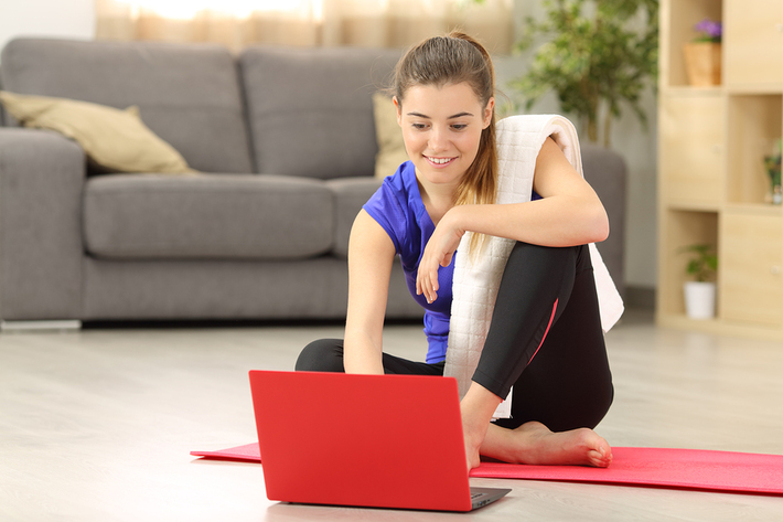 woman sitting on the floor on a yoga mat with a laptop.