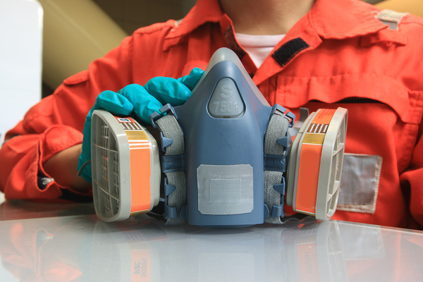 Person in an orange work suit holding a respirator.