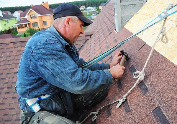 Man working on a roof with a safety strap around his waist.