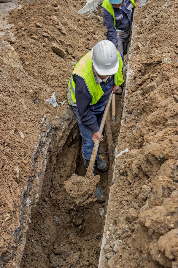 Construction workers with yellow vests and hardhats digging in a trench.