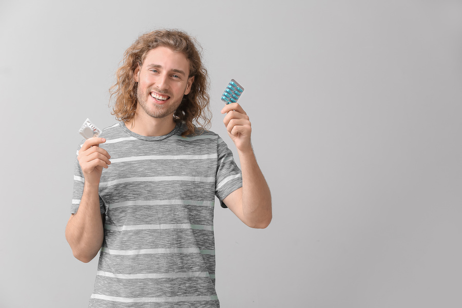 Holding a a blue pill packet and condom.