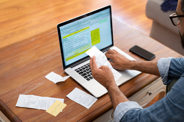 Person typing on a laptop computer while looking at sales receipts.