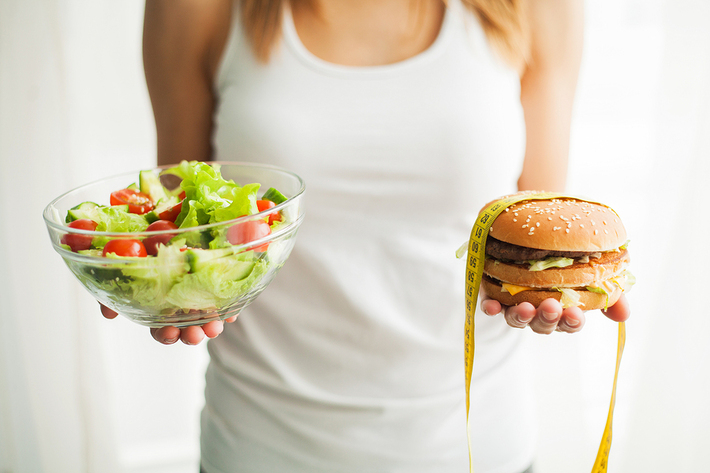 Woman holding a hamburger in one hand and a salad in the other.