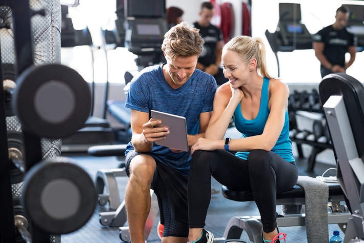 Woman and man in a fitness gym looking at a tablet together.