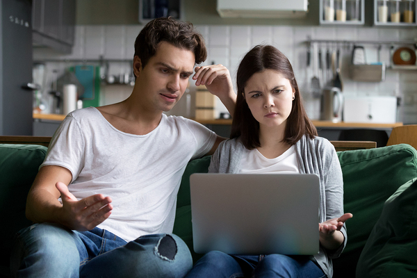 Couple sitting on a couch looking at a laptop.