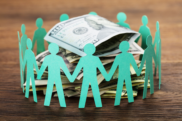 Paper cutouts of human figures in a circle around a pile of US paper money.