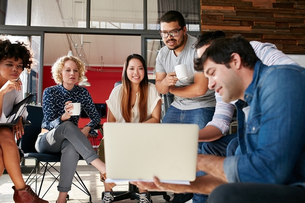 Group of colleagues sitting around a circle looking at information displayed on a laptop computer.