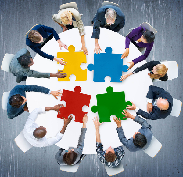 Group of people sitting around a circle table placing puzzle pieces together.