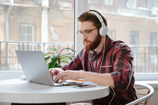 Man sitting at a table with headphones working on a laptop.