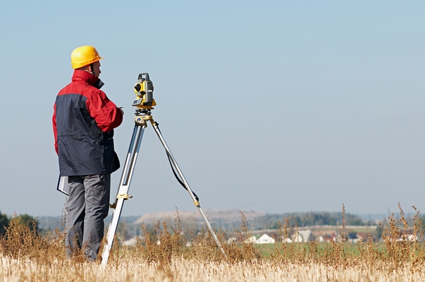 Man in a yellow hard hart surveying on a hill.