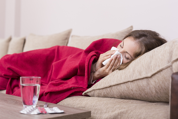 Woman lying on the couch blowing her nose with a tissue.