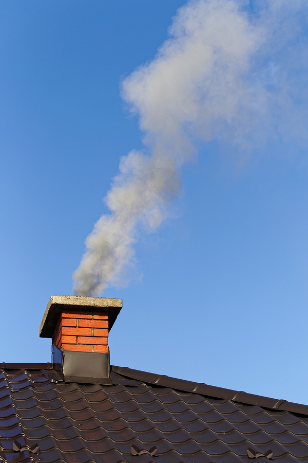 Chimney on a roof with smoke coming out of it.