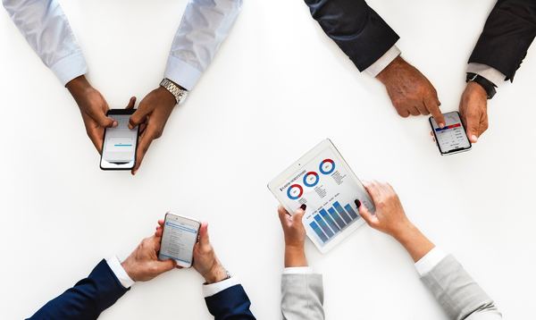 Group of people around a table using their cell phones and tablets to look at data.