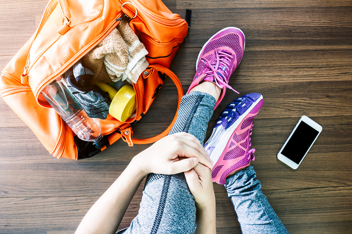 Person sitting on the floor with their gym bag and mobile phone.