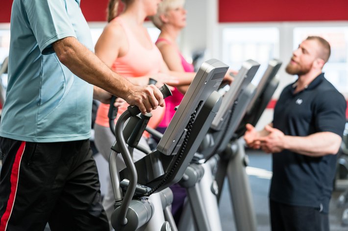 Group of people working on on treadmills with a personal trainer nearby.