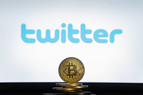 Gold coin with bitcoin symbol and twitter logo in the background.