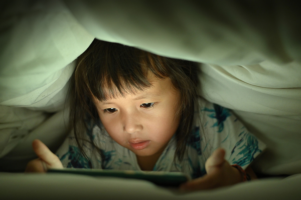 Young child looking at a tablet screen under blankets.