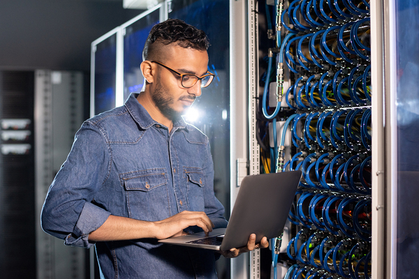 Man standing with a laptop in a server room.