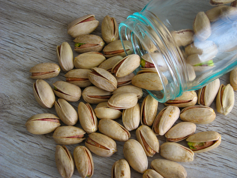 Pistachios pouring out of a glass container.