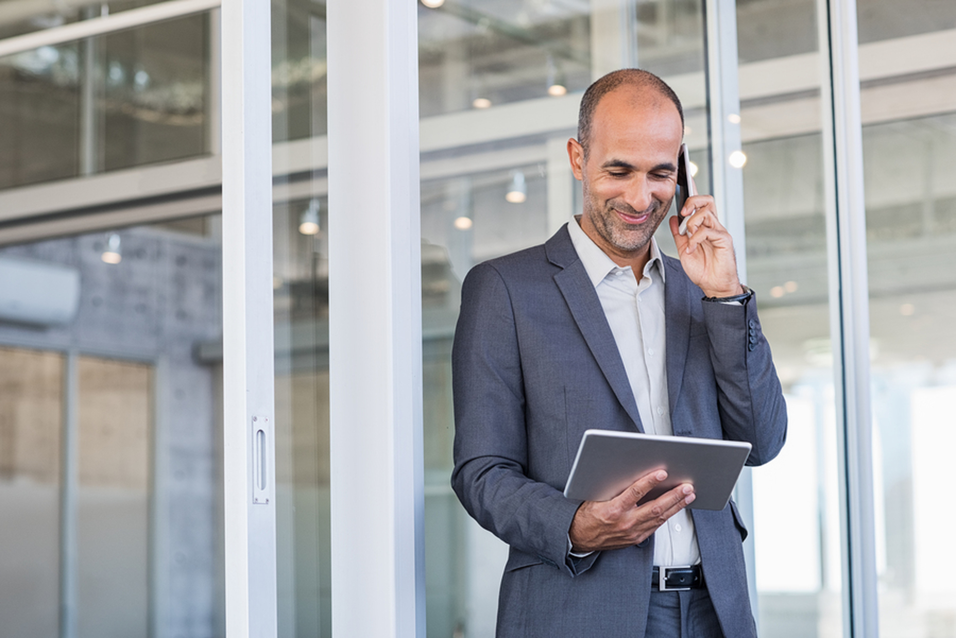 Man in a business suit talking on his phone while looking at his tablet.