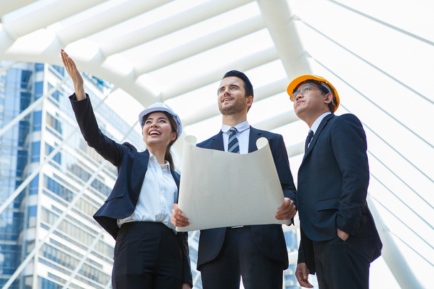 Three architects inside a glass building looking at plans.