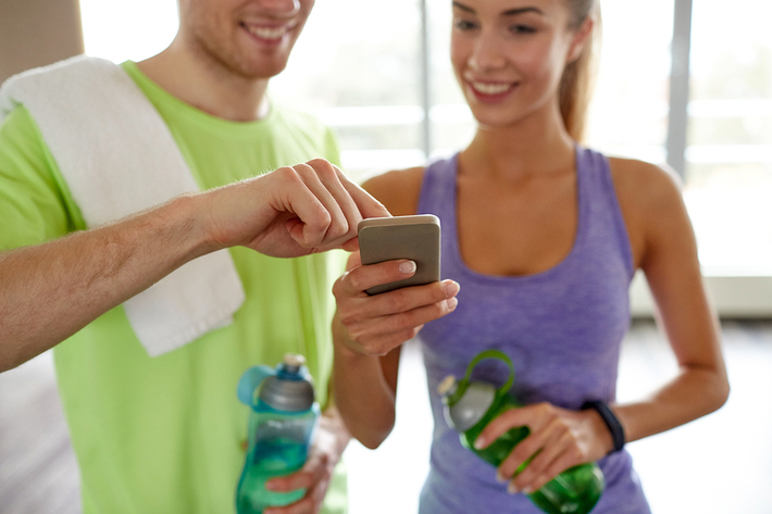 Woman in a gym getting assistance from a trainer on her mobile phone.