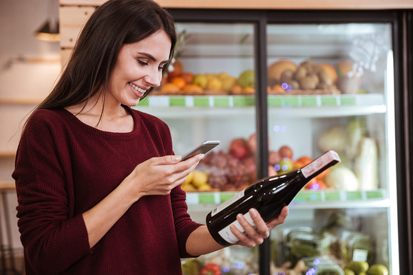 Happy woman looking at her phone and a bottle of wine.