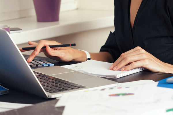 Woman working with a calculator, laptop, and notebook.
