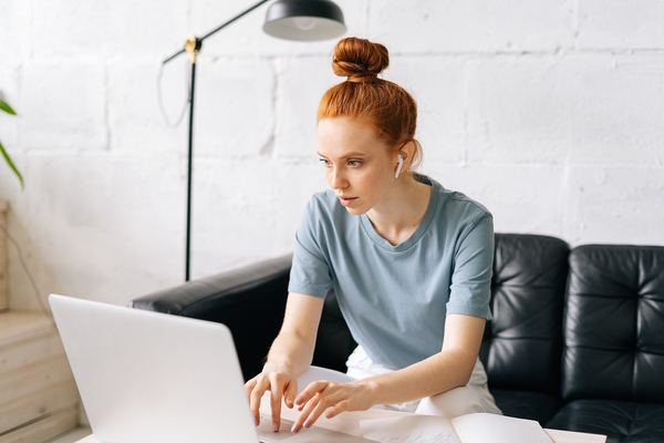 Woman sitting on her couch typing on a laptop.