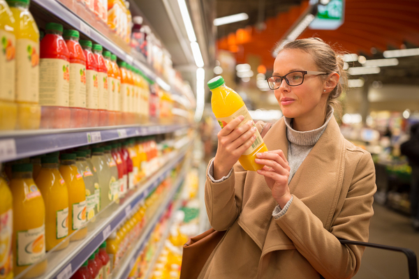 Woman shopping in a grocery store holding a bottle of orange juice.