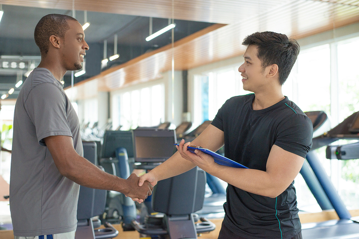 Man shaking hands with a person trainer in a gym.