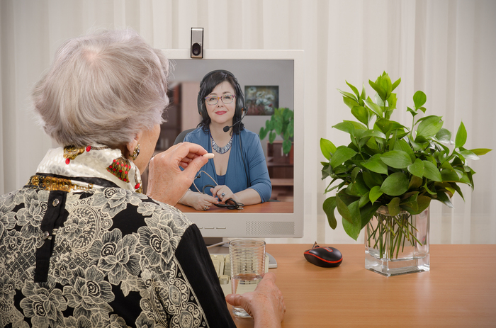 Elderly woman taking medication while consulting a medical professional in a video conference.