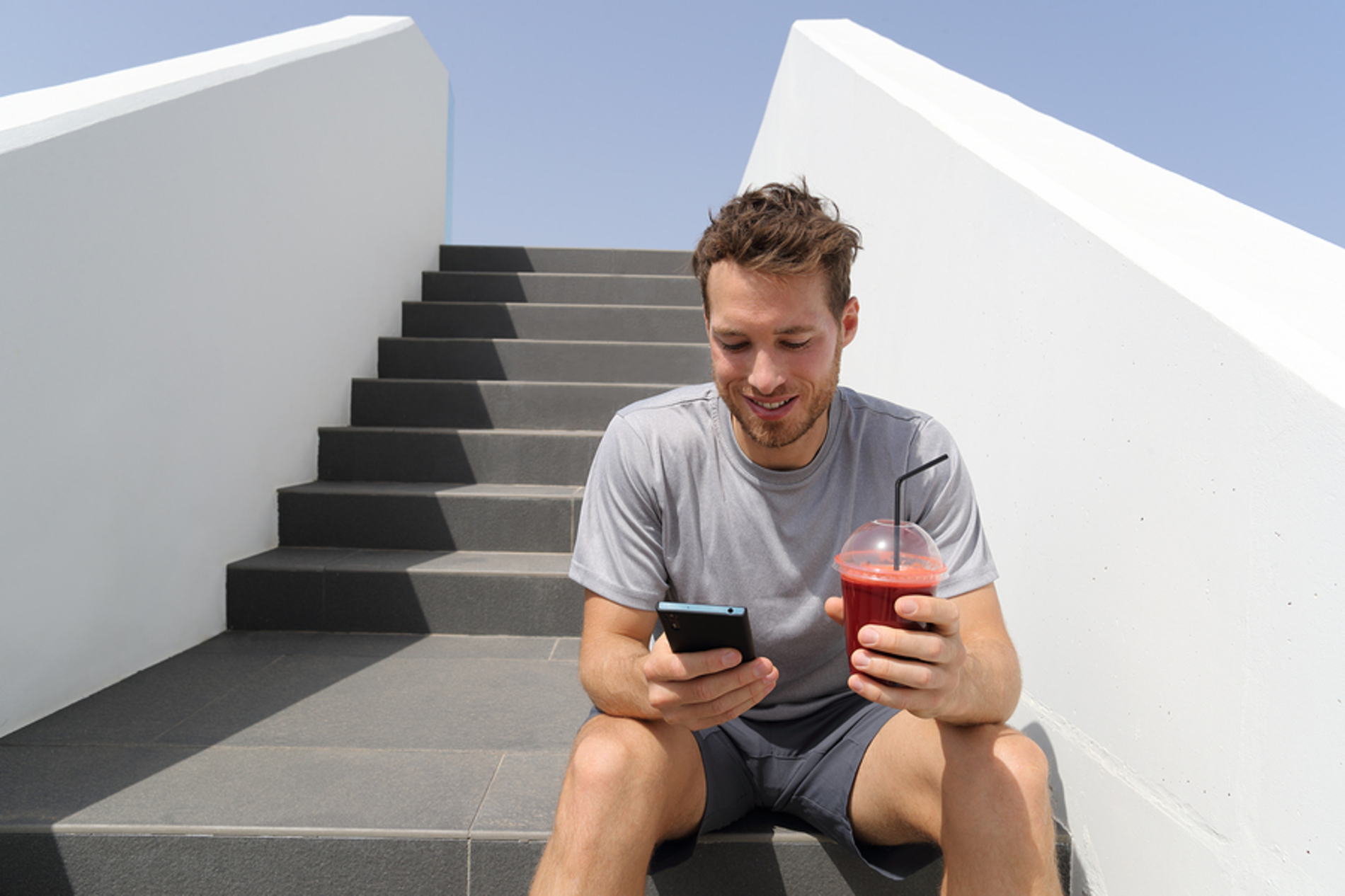 Man sitting on steps with his phone and a drink. Man sitting on steps with his phone and a drink.