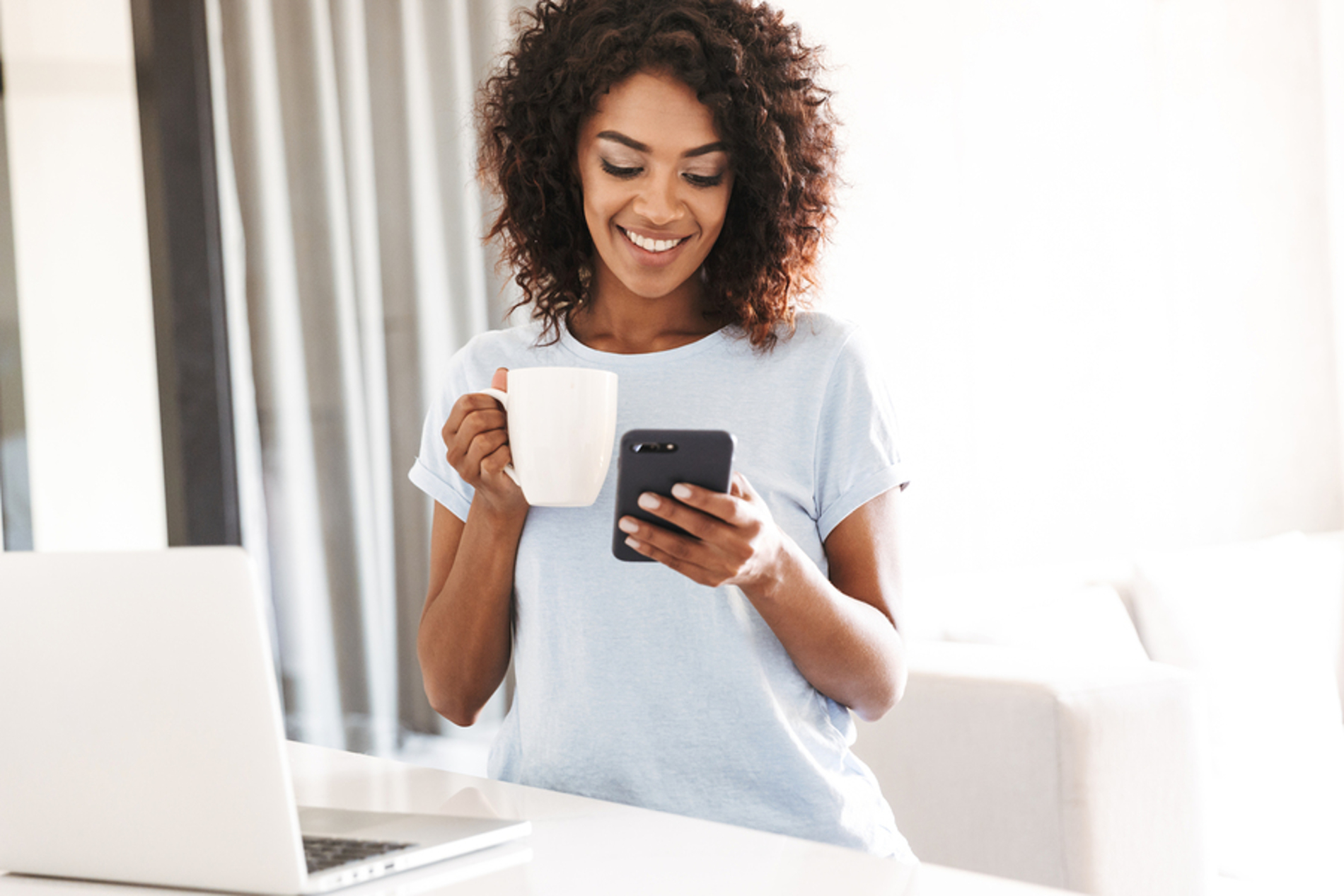 Woman looking at her phone while drinking a cup of coffee.