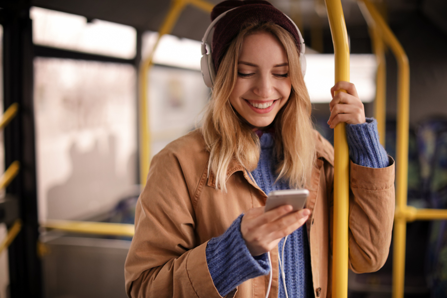 Woman standing in public transportation listening to a podcast on her phone.