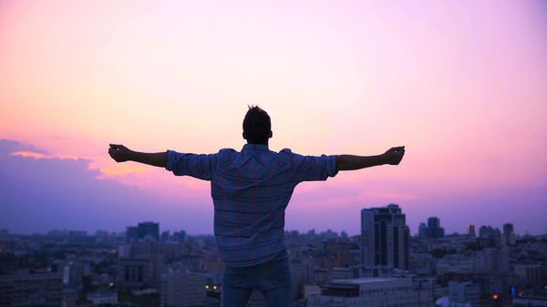 Man looking out at the sun rising with his arms spread out in celebration.