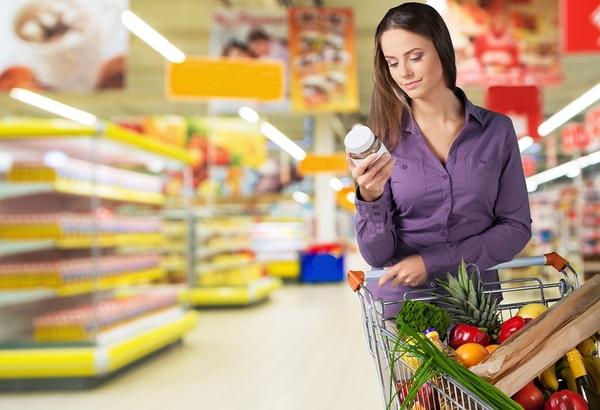 Woman shopping in a grocery store looking at a product label.