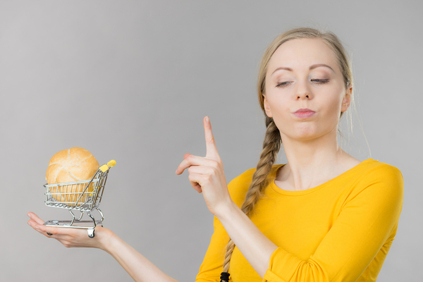 Woman holding a miniature shopping cart looking cautious.