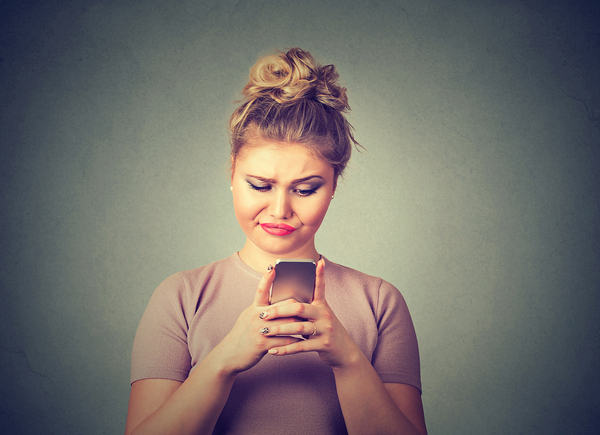 Woman looking at mobile phone making a disgusted face.