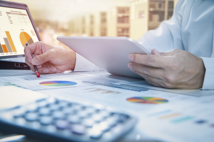 Person looking at charts and graphs on documents and a tablet.