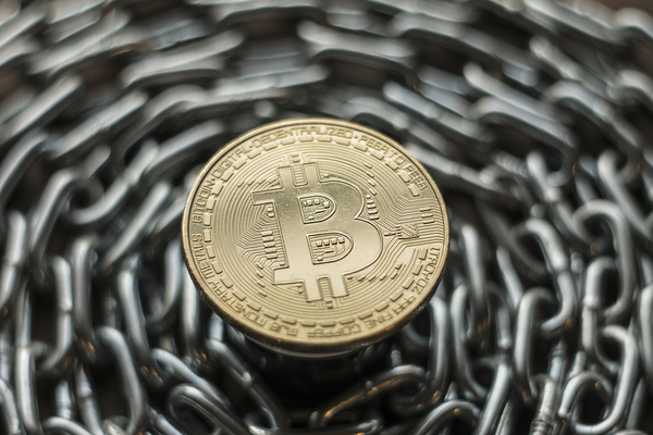 Gold bitcoin surrounded by a steel chain to illustrate a DAO